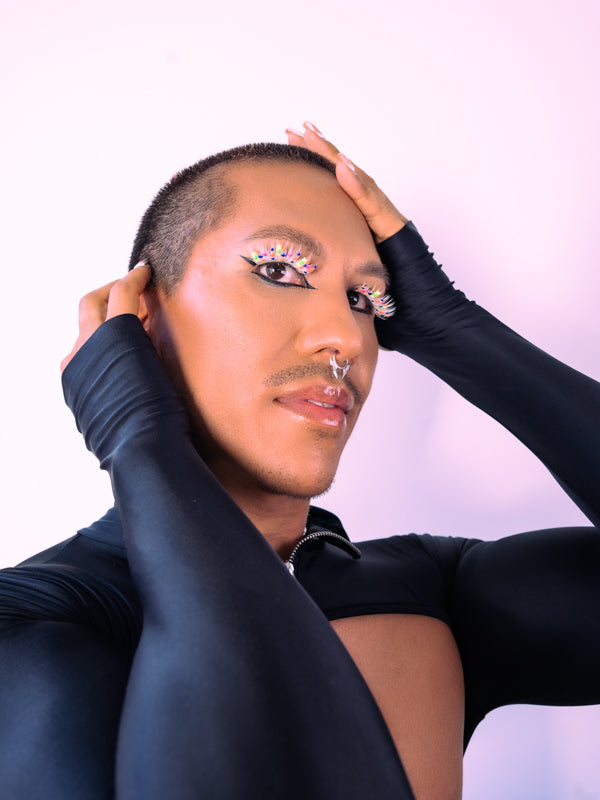 A gorgeous model poses with hands by his face. He paired silver flame-shaped nose jewelry with custom-made white Sparkle lashes by BFlare Beauty and a bold black eyeliner..