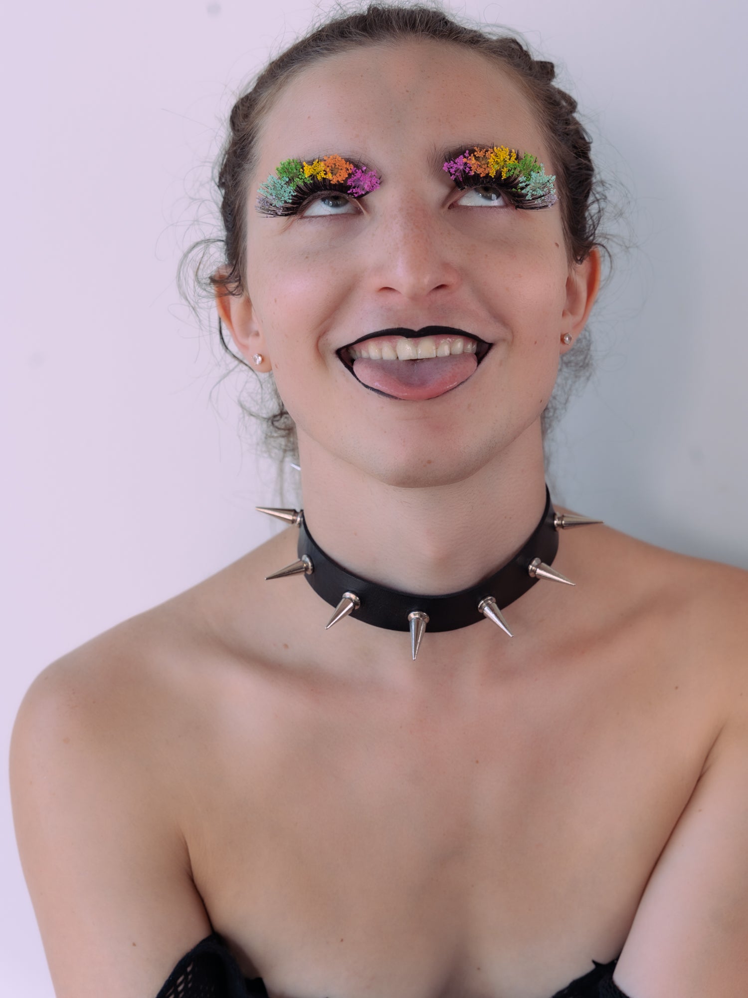 Our gorgeous model is seen from the chest up, wearing a strapless top and black and chrome spiky collar. She's sporting black lipstick and a pair of rainbow Bloom Lashes by BFlare Beauty. 